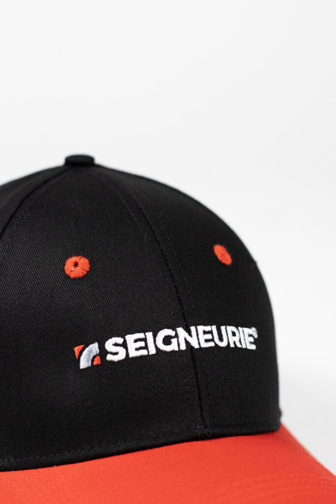 Casquette noire et rouge avec logo Seigneurie brodé en blanc, contraste fort et marquage textile professionnel. Focus broderie.
