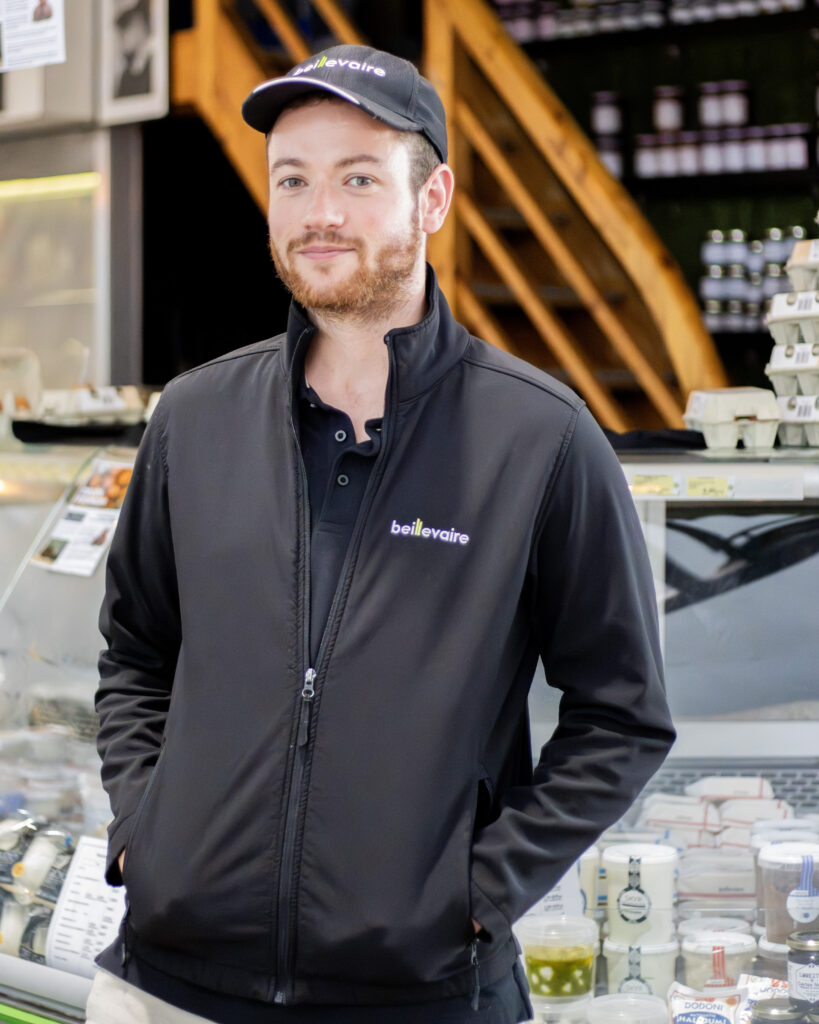 Employé en boutique alimentaire portant une veste softshell noire personnalisée Beillevaire et une casquette logotypée, tenue professionnelle brodée pour équipe magasin.
